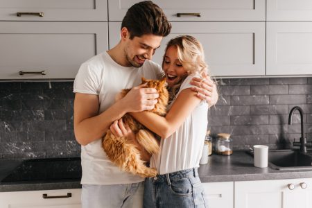 Stunning curly girl holding fluffy cat. Indoor photo of european couple playing with their pet.